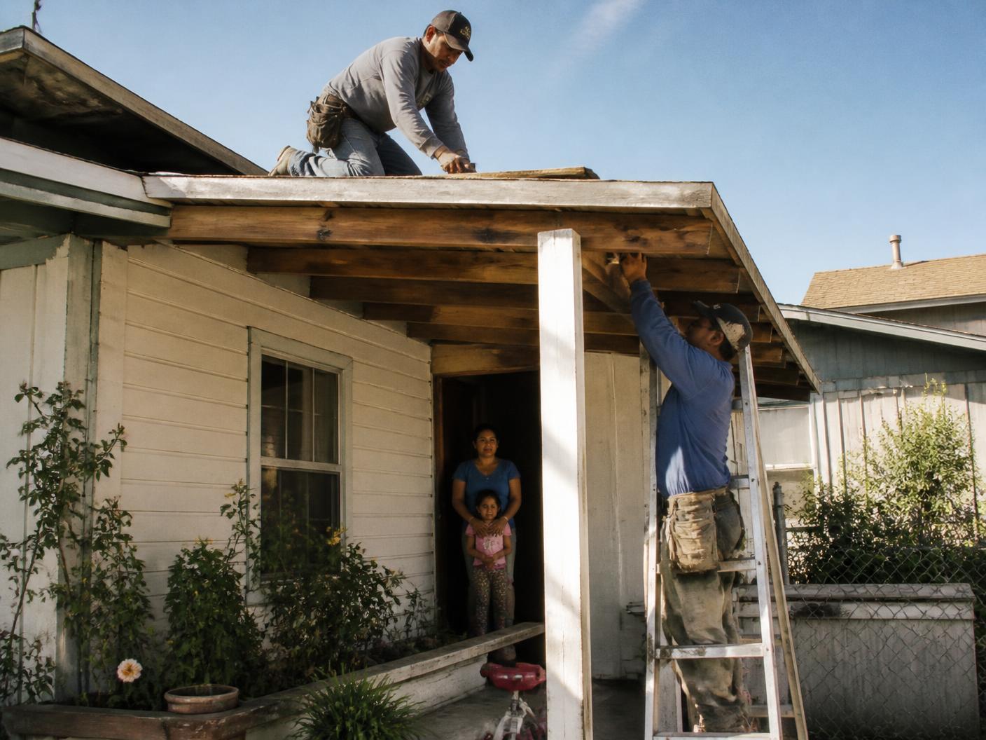A volunteer repairing a damaged section of a family home while the household looks on